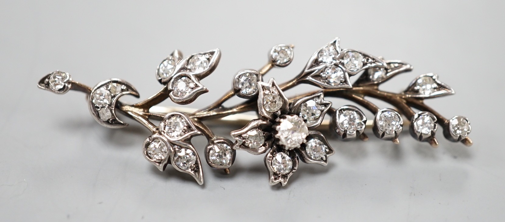 A yellow metal and diamond cluster set foliate spray brooch, 47mm, gross weight 4.5 grams.